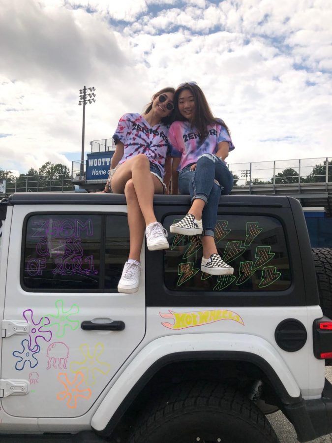 Eleni Jones and Rachel Son sitting on top of one of the cars they painted in their tie-dye senior shirts