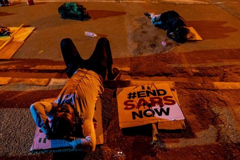 Young Nigerian protesters lay next to their signs, showing 
support for the #EndSARS movement.