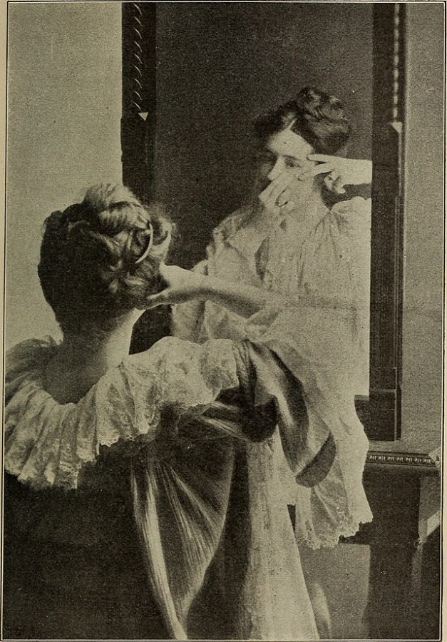 A woman in 1904 practices early skincare in the mirror.