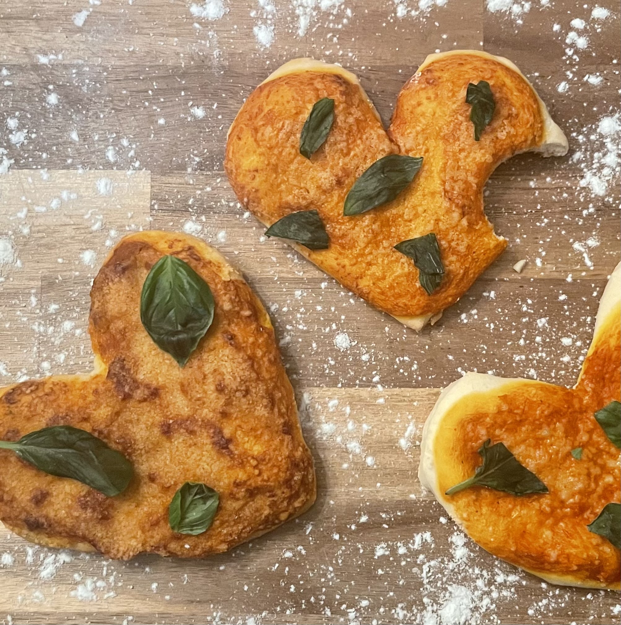 Freshly baked heart-shaped pizzas, topped with parmesan and basil are a fun and easy recipe to try.