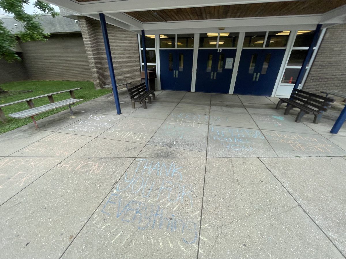 Students write messages of appreciation for teachers and staff on the sidewalk outside the auditorium.