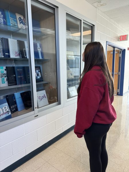 Senior Editor-in-Chief Brooke Zweig looks at the trophy case located on the second level of the school next to the pillar entrance stairs, which holds past yearbooks and awards .