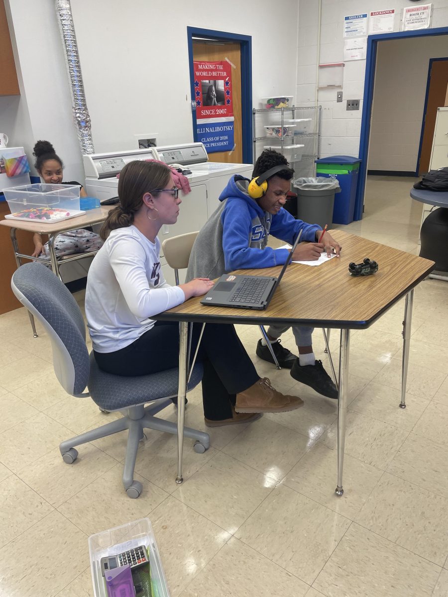 Coach Mia Krawzcel works with student Samuel Tiarami-Adeyemi in Room 175 on writing his phone number, part of his individual studies. 