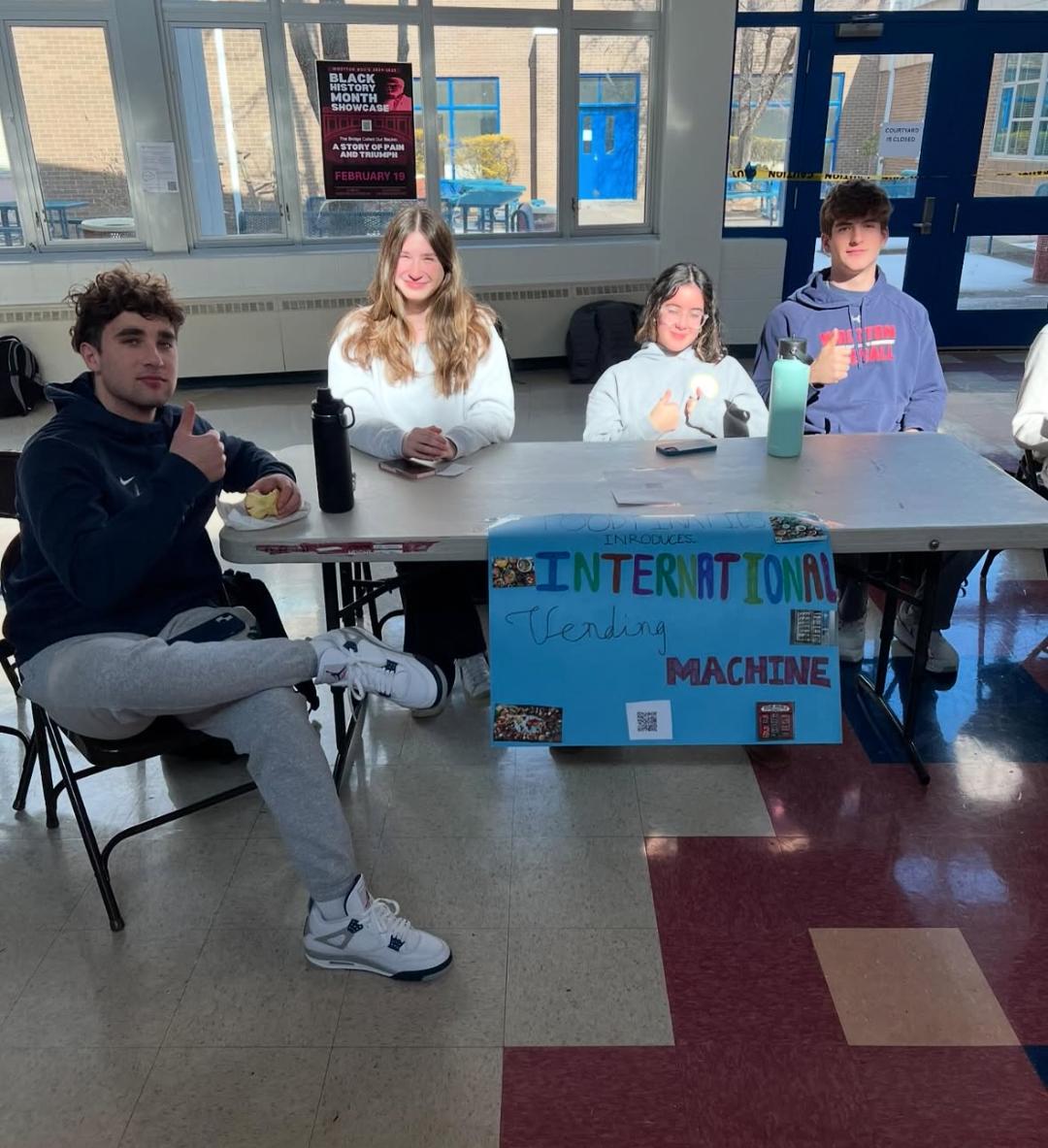 Juniors Maxwell Scherr, Addie Gorman, Natalie Asvestopoulou and senior Luke Brunner sit at their project table. The business showcase on Jan. 24 allowed them to market their international vending machine. “It was very successful and a good experience,” Asvestopoulou said.