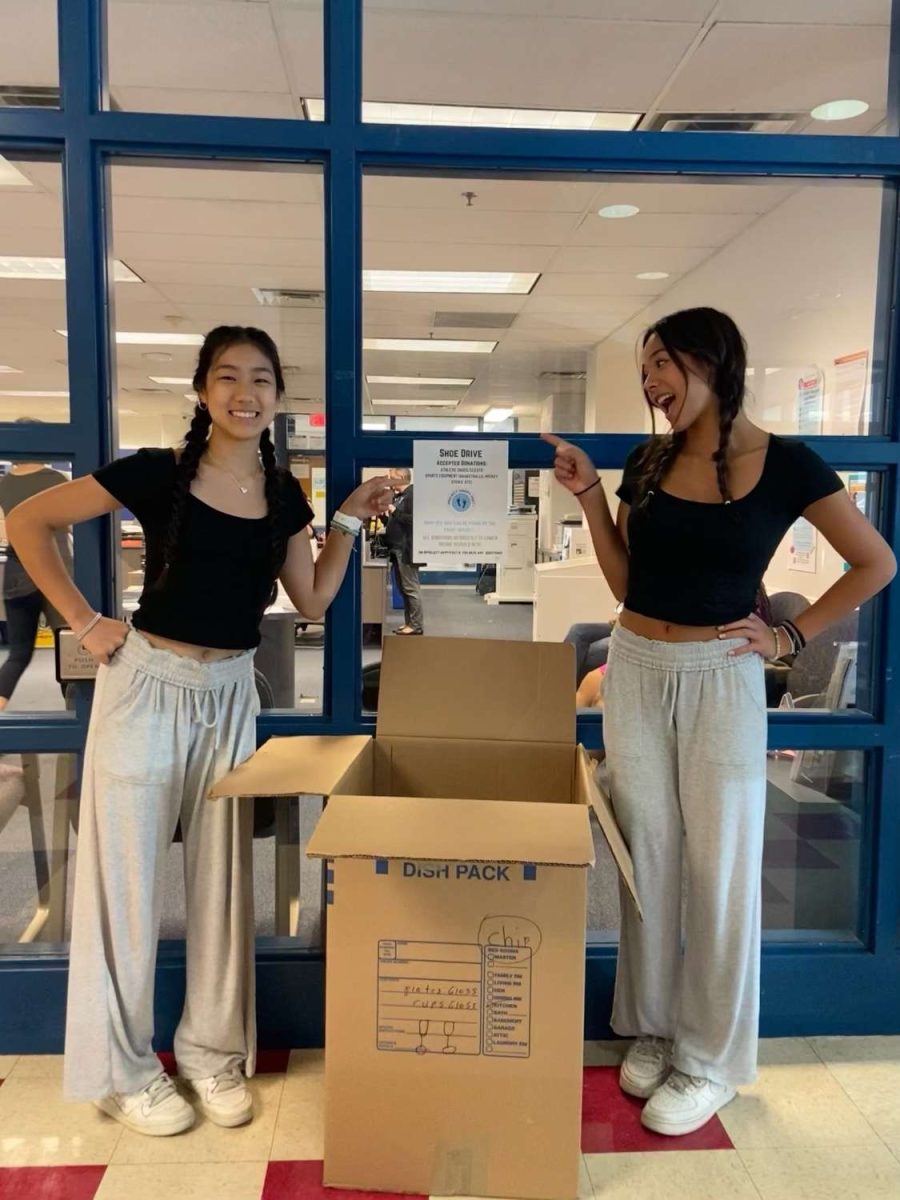 Senior leaders Emma Yuan and Cayla Schwartz stand next to their donation box to promote a shoe drive for their club, Project Happy Feet.