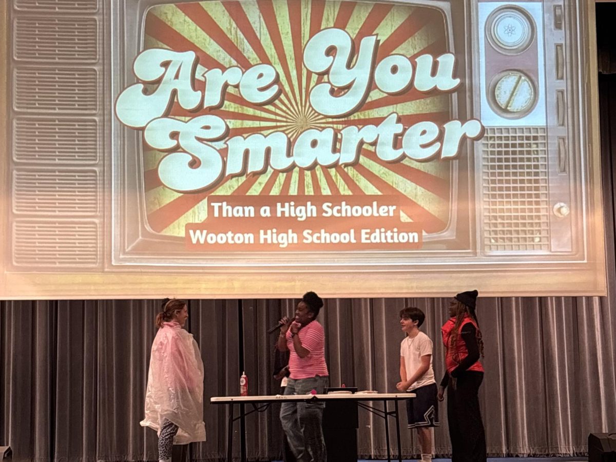 SGA representative junior Peace Tiam mediates a game of "Are You Smarter than a High Schooler?" at the town hall in the auditorium on Oct. 22. Freshman Ray Spivak and junior Zikora Okeke faced off against counselors Daniella Bienstock and Sheri Snyder. The staff won 2-1 against the students, leading to Spivak and Okeke being pied in the face. "During town halls, it's very easy to get distracted or disengaged, but having interesting games brings the attention back to the stage, and it keeps their minds sharp and active," co-head of SGA's town hall committee, senior Urielle Ngako said. Photo by Amal Shaikh